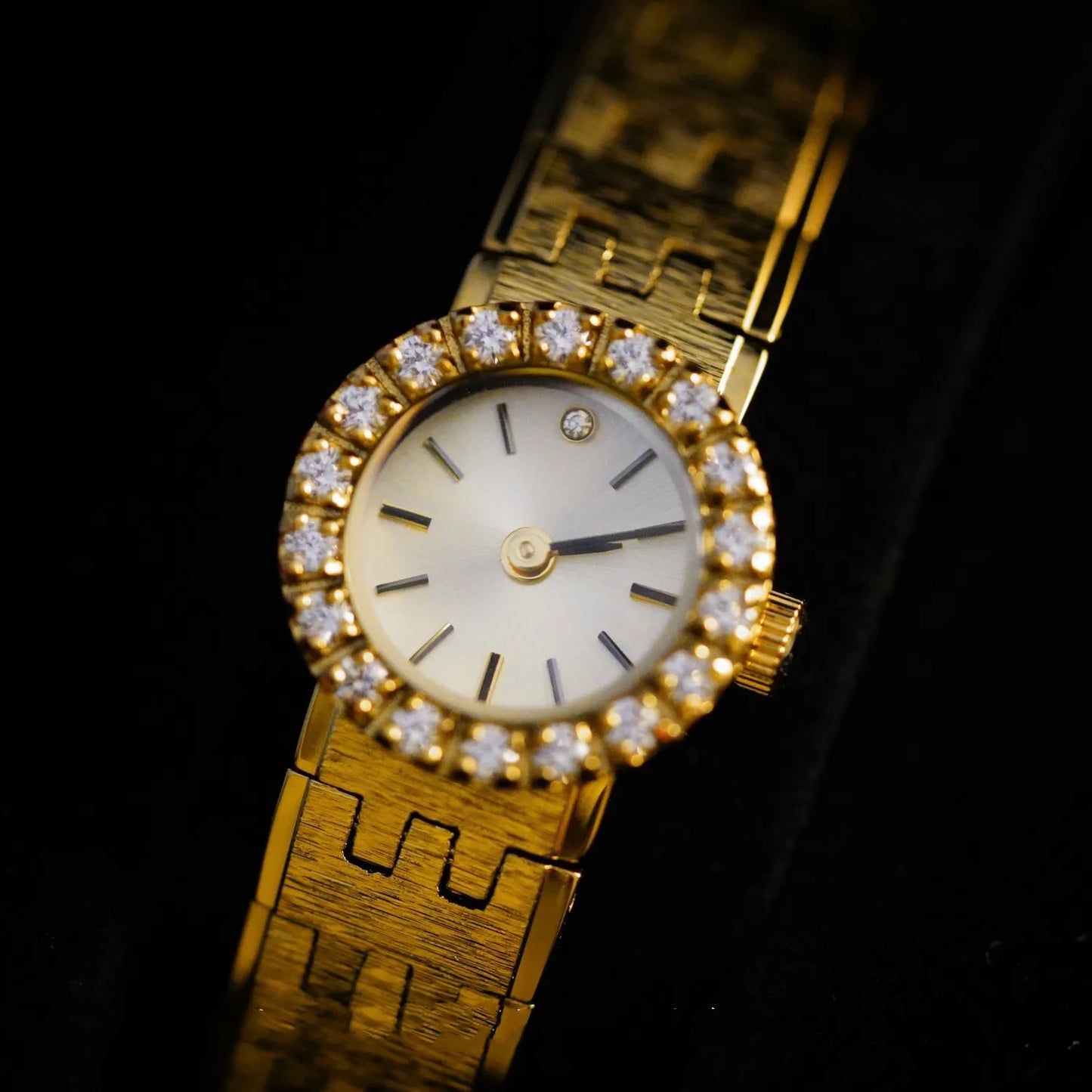 brushed gold band with a round face. there are no numbers on the face of the watch. diamonds around the outside of the watch with a diamond at 12 o'clock. comes with a safety chain. vintage elegance