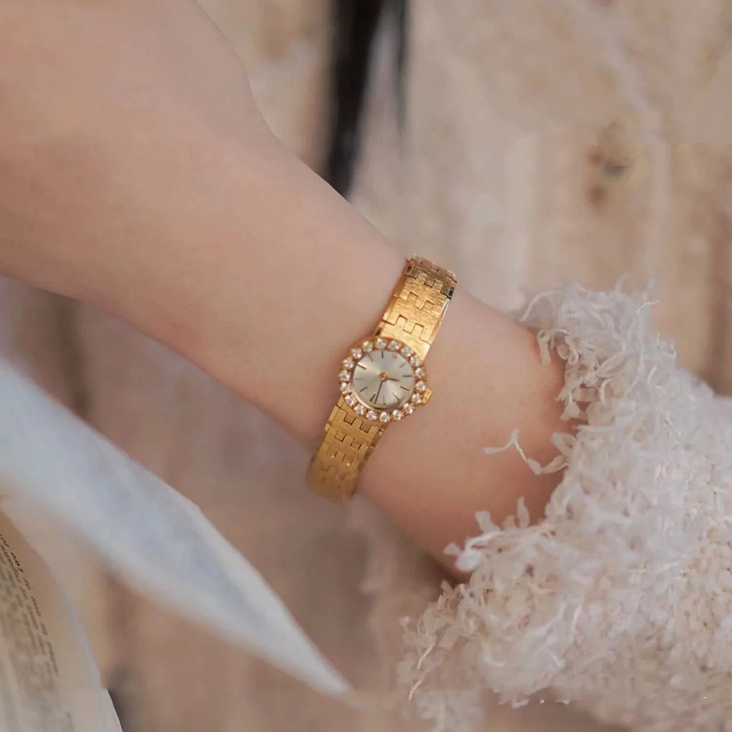 brushed gold band with a round face. there are no numbers on the face of the watch. diamonds around the outside of the watch with a diamond at 12 o'clock. comes with a safety chain. vintage elegance