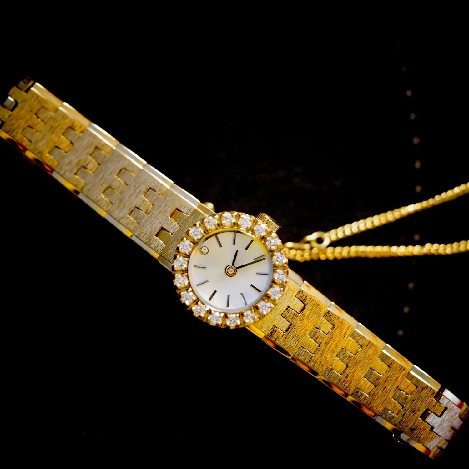 brushed gold band with a round face.  there are no numbers on the face of the watch.  diamonds around the outside of the watch with a diamond at 12 o'clock.  comes with a safety chain.  vintage elegance