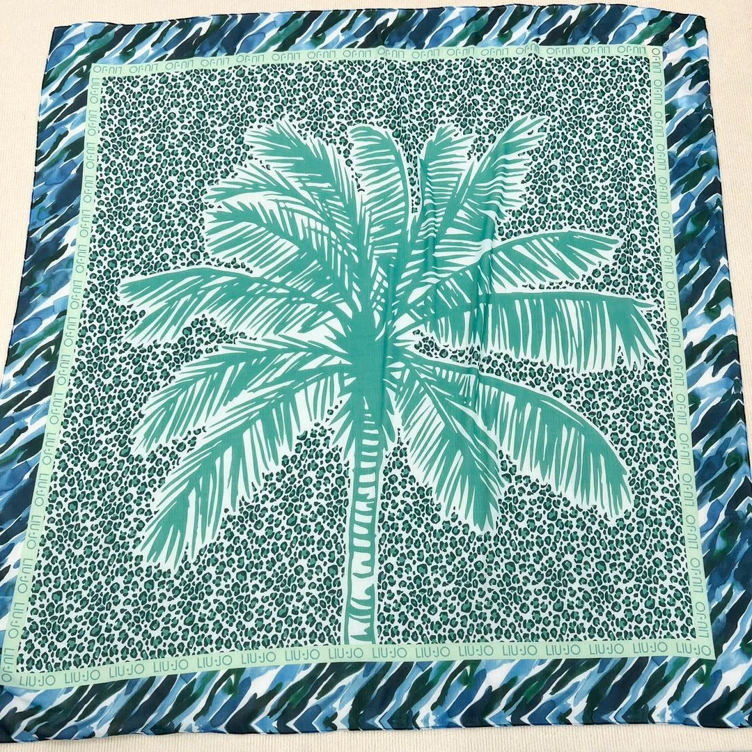 Stay protected from the harmful rays of the sun with our Italian Original Sunscreen Shawl. Its lightweight and stylish design make it the perfect addition to your summer wardrobe. Enjoy your time at the beach or pool without worrying about sunburns. A must-have for any sunny day! The motif is a large palm tree on a turquoise leopard print rectangle inside blue and green and white abstract stripes.  the leopard is bordered in green Liu-Jo