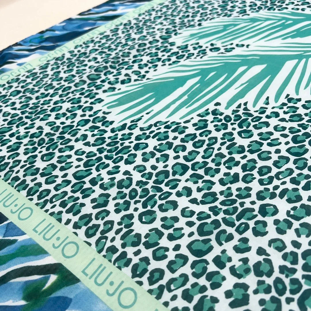 The motif is a large palm tree on a turquoise leopard print rectangle inside blue and green and white abstract stripes. the leopard is bordered in green Liu-Jo